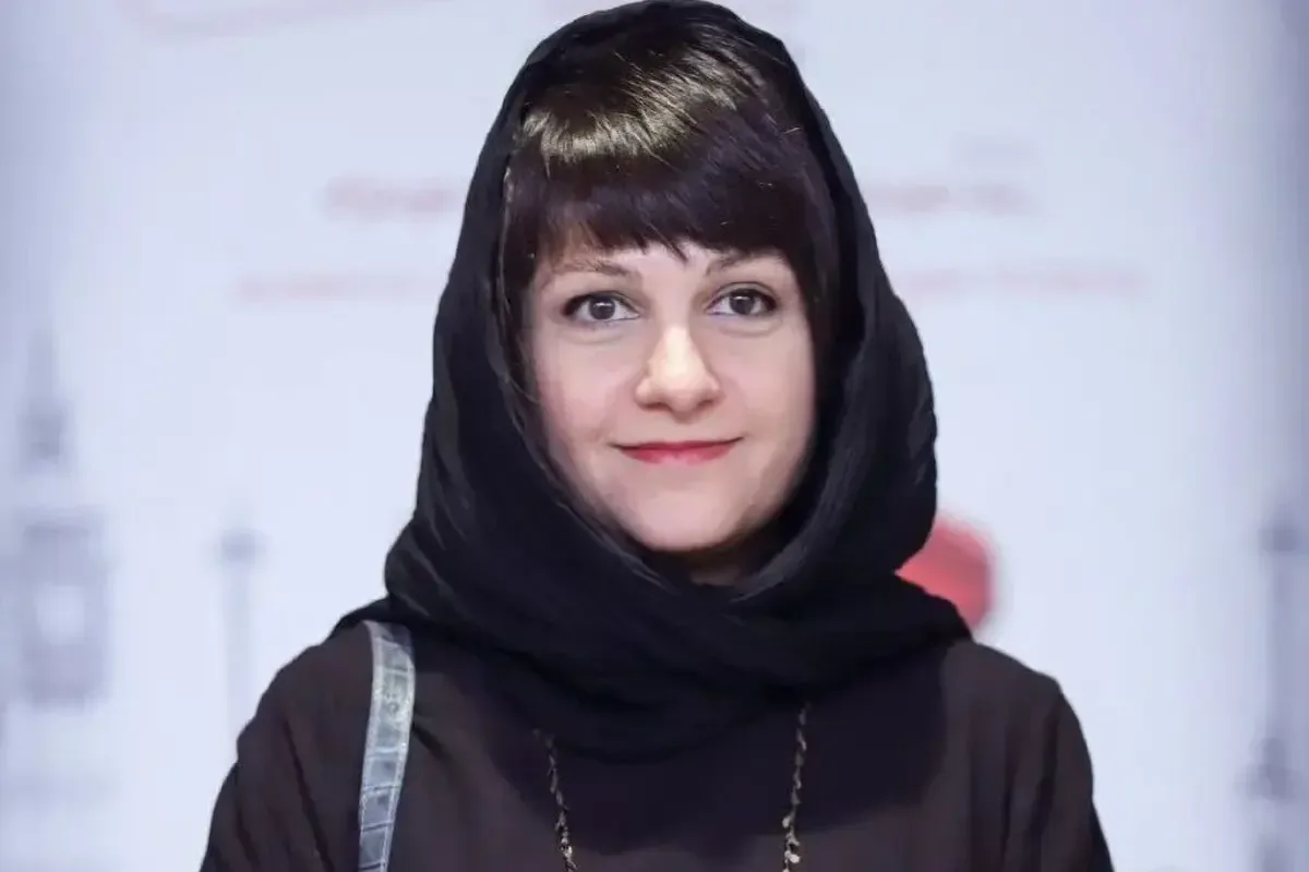 آیدا پناهنده با روسری مشکی و لباس تیره مقابل پس‌زمینه روشن