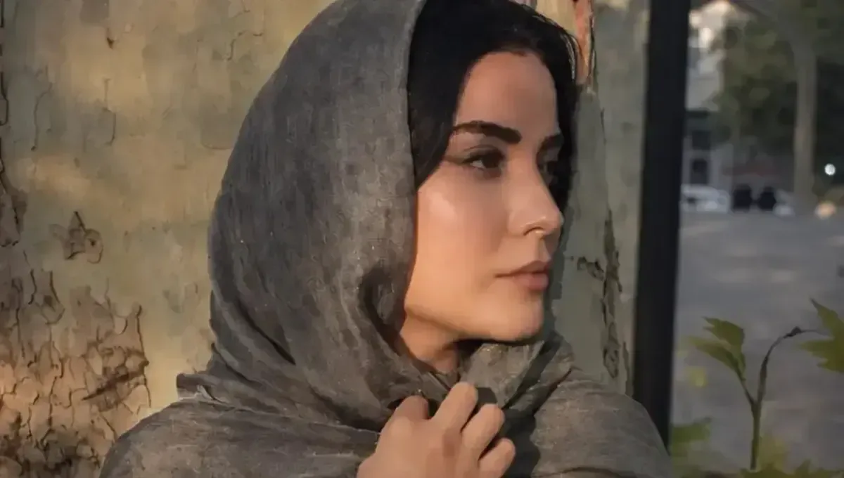 نیمرخ عاطفه حبیبی با شال خاکستری کنار تنه درخت