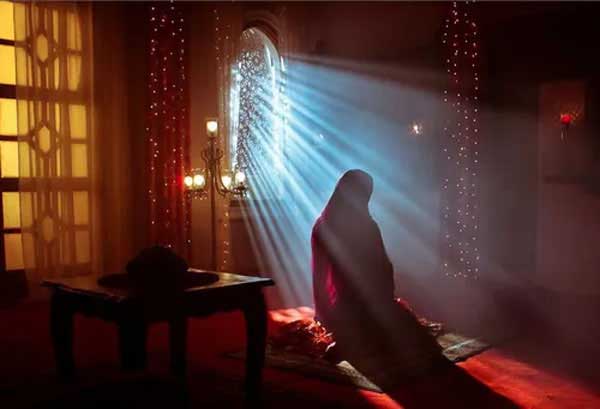 نمازگزار در حال عبادت نمازگزار با چادر در برابر نور پنجره